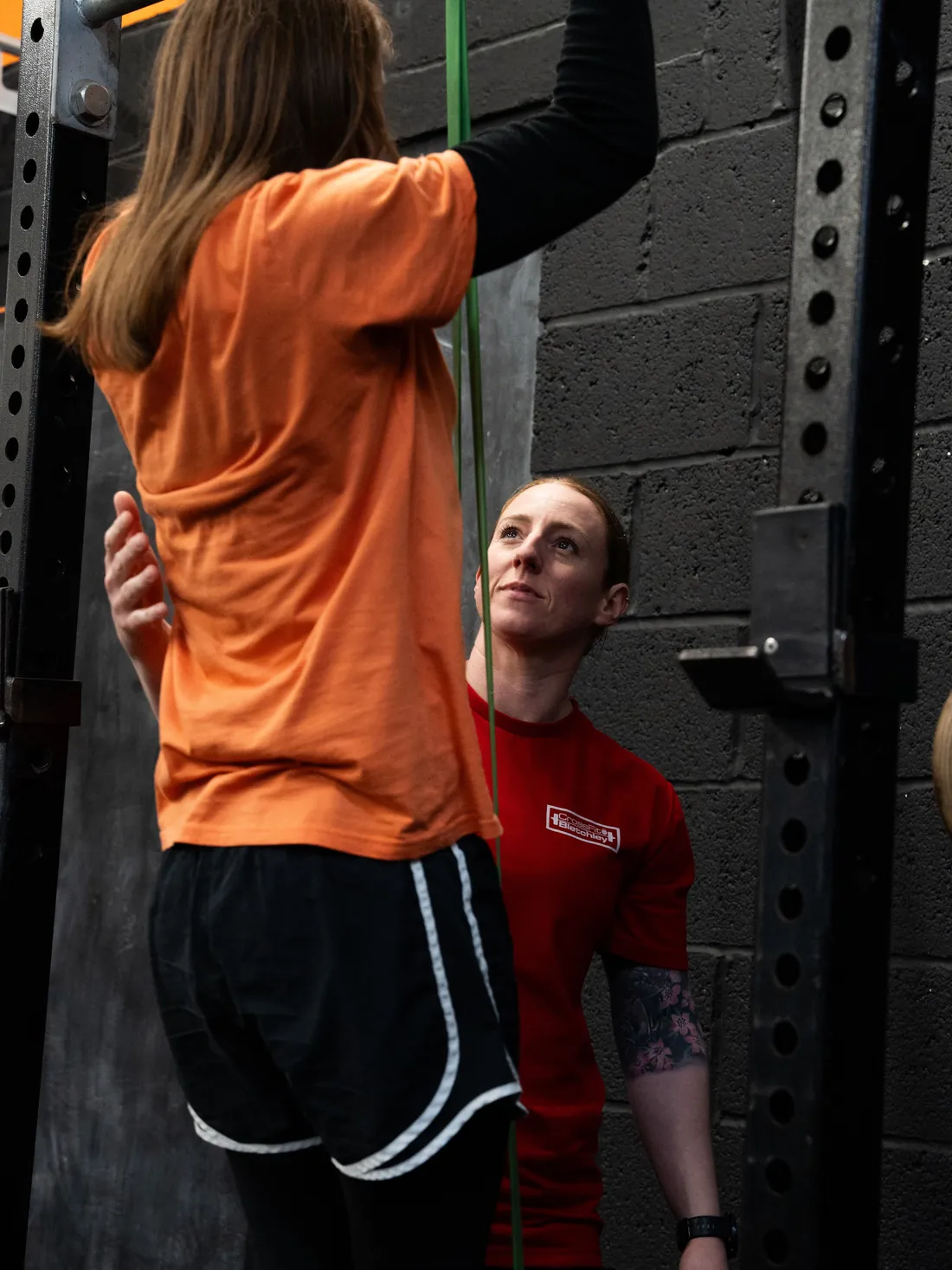 A coach supporting a member through banded pull-ups